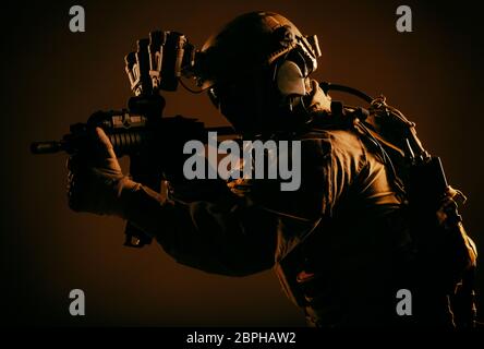 Army elite forces soldier, special security service fighter in tactical gear and ammunition, night vision device on helmet, aiming short barrel rifle, Stock Photo