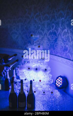 A pyramid of champagne glasses stand on the table. The table is covered with a white tablecloth. The pyramid is highlighted in blue. Stock Photo