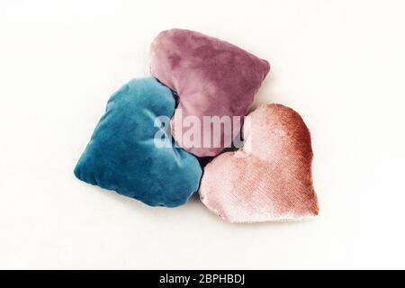 Three heart shaped pillows made up from velvet. Love gifts for couples. Rose, teal and purple colors. White background Stock Photo