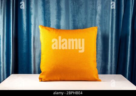 Horizontal shot of an orange pillow on the desk. Blue velvet background. Light casting soft shadows on the table. Interior design idea Stock Photo