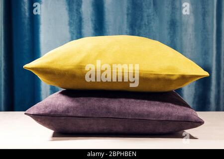 Yellow and purple pillows standing one on to another. Blue velvet background. Soft light coming from the top, Warm whitebalance Stock Photo