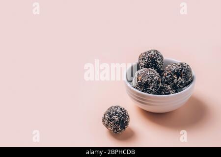 Healthy energy balls made of dried fruits and nuts with coconut chips, flax seeds, pistachios, sesame. Raw vegan candy in white bowl on pink background. Stock Photo