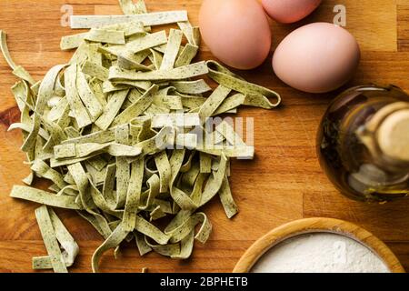 Raw italian pasta with eggs and flour. Dry noodles with spinach on wooden table. Top view. Stock Photo