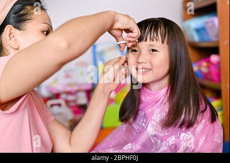 Asian Mother cutting hair to her daughter at home while stay at home safe from Covid-19 Coronavirus during lockdown city. Self-quarantine and social