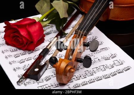 St.Petersburg, Russia - November 2016 - Violin (fiddle) with red rose lying on the sheet of music on a black background. String instrument. Stock Photo
