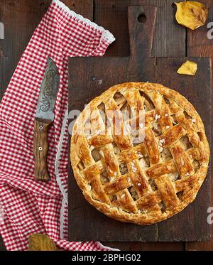 Baked whole round apple pie on a rectangular old brown board, wooden table, top view Stock Photo