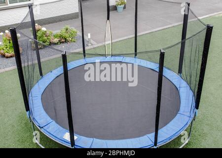 Blue trampoline with safety net on the lawn in garden outdoors for children Stock Photo
