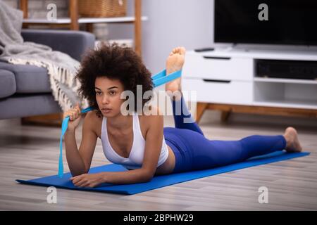 Serious Young Woman In Sportswear Doing Workout With Yoga Belt At Home Stock Photo