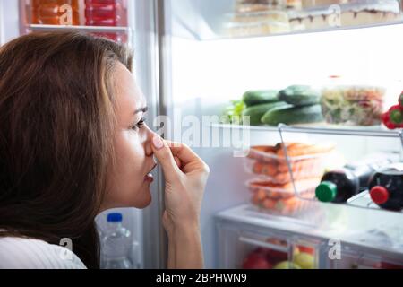 Side View Of Young Woman Recognizing Bad Smell Coming From The Refrigerator Stock Photo