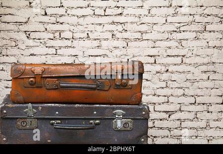 Close up stack of two old vintage antique grunge travel luggage brown leather suitcase trunks isolated over background of white brick wall, low angle Stock Photo