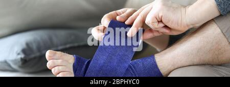 Man sits at home couch and bandages foot bandage Stock Photo