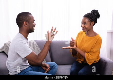 Smiling Young Couple Sitting On Sofa Communicating With Sign Languages Stock Photo