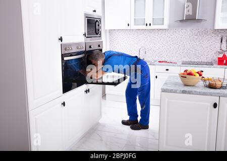 Mature Technician In Overall Repairing Oven In Kitchen Stock Photo