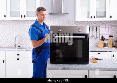 Mature Male Technician Repairing Oven On Kitchen Worktop Stock Photo