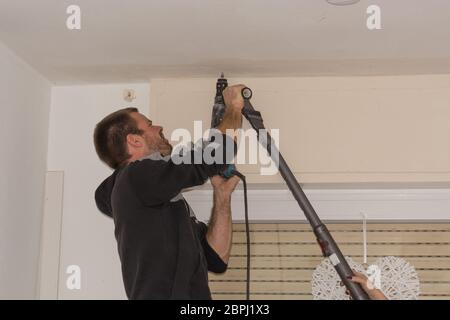 The man drills a hole in the ceiling before mounting a curtain rod Stock Photo