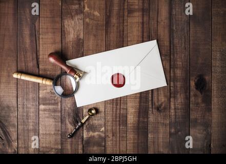 Blank paper envelope with red wax seal, stamp, spoon and magnifier on wooden background. Mockup for your design. Flat lay. Stock Photo