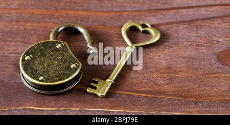 Gold vintage heart key and unlocked padlock on wooden background. Sweet home concept, web banner. Stock Photo