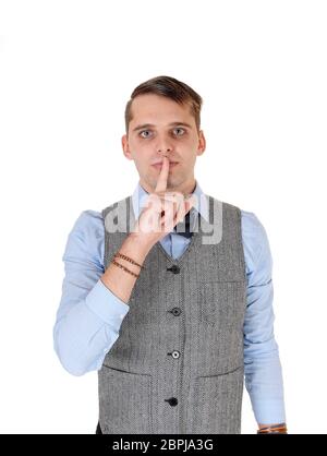 A handsome young man standing in blue shirt and gray vest holding his middle finger over his mouth, be quiet, isolated for white background Stock Photo