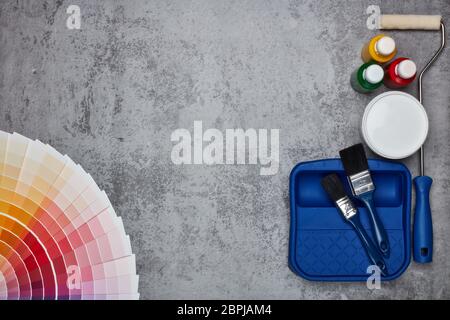 Color palette guide and painting accessories ( paint brushes, roller and cans of paint) on grey background. Top view with copy space,  Concept of cons Stock Photo