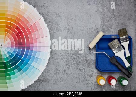 Color palette guide and painting accessories ( paint brushes, roller and cans of paint) on grey background. Top view with copy space,  Concept of cons Stock Photo