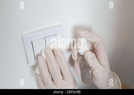 Woman wiping light switcher with antibacterial disinfecting spray Stock Photo