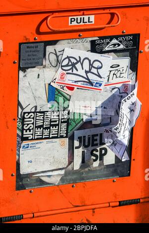 Orange free newspaper dispenser covered in stickers in New York City, United States of America Stock Photo