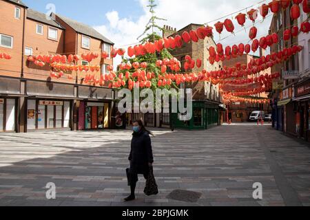 Woman wearing a face mask walks under red lanterns through Chinatown, which is eerily quiet and silent on empty streets as lockdown continues and people observe the stay at home message in the capital on 11th May 2020 in London, England, United Kingdom. Coronavirus or Covid-19 is a new respiratory illness that has not previously been seen in humans. While much or Europe has been placed into lockdown, the UK government has now announced a slight relaxation of the stringent rules as part of their long term strategy, and in particular social distancing. Stock Photo