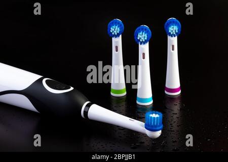 Electric rechargeable toothbrush with three toothbrush heads on black background with water drops. Focus on the power button. Stock Photo