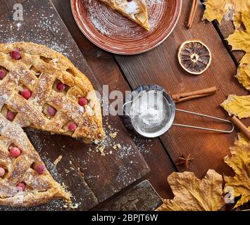 round apple pie on a rectangular old brown cutting board sprinkled with powdered sugar, top view Stock Photo