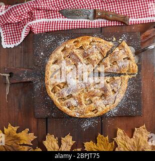 Baked whole round apple pie on a rectangular old brown board, wooden table, top view Stock Photo