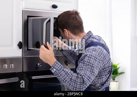 Side View Of Young Man Repairing Microwave Oven In Kitchen Stock Photo