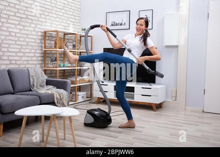 Happy Female Janitor Dancing With Vacuum Cleaner At Home Stock Photo