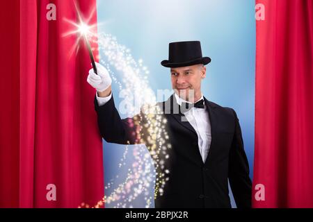 Happy Mature Magician Wearing Black Hat Doing Magic With Illuminated Wand Stock Photo