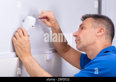 Close-up Of Male Electrician Installing Security System Door Sensor On Wall Stock Photo