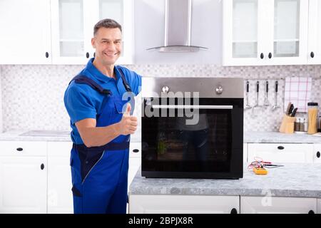 Mature Male Technician Repairing Oven On Kitchen Worktop Stock Photo