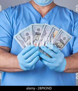 doctor in blue uniform and latex sterile gloves holds a lot of paper money, the concept of corruption in medicine Stock Photo
