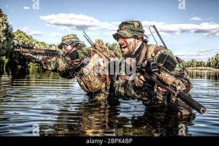 Pair of soldiers in action during river raid in the jungle waist deep in the water and mud and covering each other Stock Photo