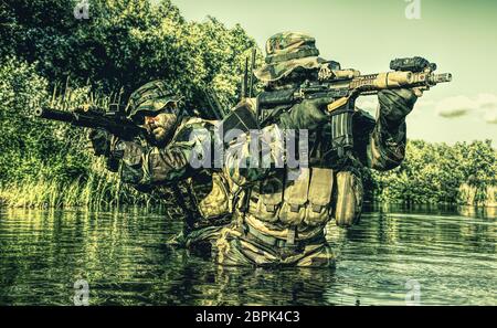 Pair of soldiers in action during river raid in the jungle waist deep in the water and mud and covering each other Stock Photo