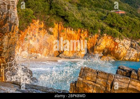 Summer evening on a small beach among the rocks. The roof of the cottage among the dense forest. Surf spray Stock Photo