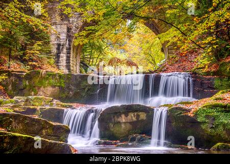 Autumn day in the sunny forest. Old stone bridge. Small river and several natural waterfalls Stock Photo