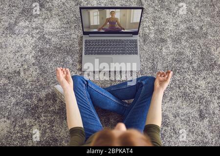 Online yoga meditation. Girl in casual clothes is practicing yoga meditation in room. Stock Photo