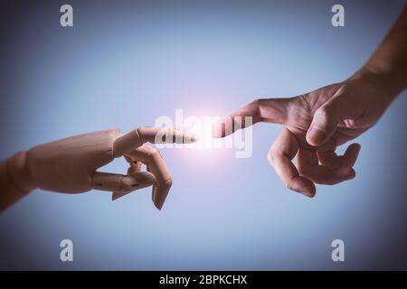 Photograph of a human hand and a hinged wooden hand. Concept image of The Creation Of Adam. Stock Photo
