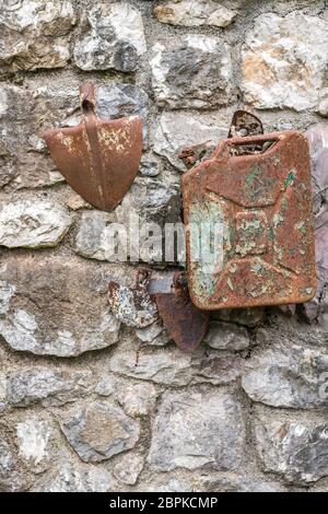Old decaying rusty gasoline canister and shovel head attached to a wall of a building in a countryside Stock Photo