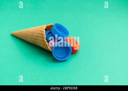 Plastic free and unnatural plastic food concept. Waffle cone with plastic bottle caps on green background Stock Photo