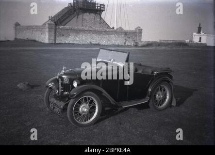 Small two-seater open-top sports car parked on grass opposite an old coastal dwelling, South-East England, UK, circa, 1946-1950. Stock Photo