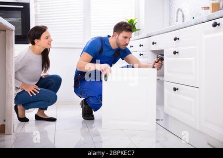 Woman Looking At Male Handyman Installing Cabinet Door In The Kitchen Stock Photo