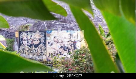 Nine Mile, Jamaica JANUARY 07, 2017: Graffiti wall outside of the Bob Marley Mausoleum compound, view from behind of palm leaves Stock Photo