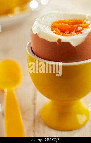 Close-up on open soft-boiled organic egg in yellow ceramic eggcup served with plastic spoon Stock Photo