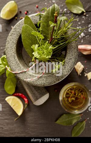 Fresh mixed herb bouquet garni in a stone pestle and mortar with oil, spices and lemon on a rustic table Stock Photo