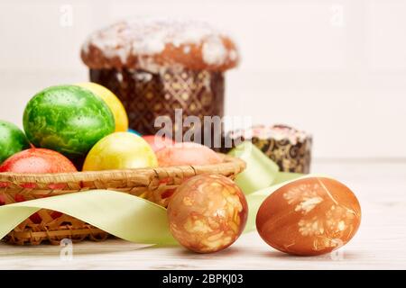Still life with colored easter eggs and easter cakes  lying  on a  wooden table on light  background. Greeting card. Selective focus on eggs Stock Photo